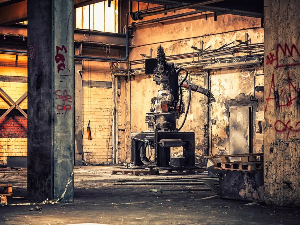 A large industrial robot in a dilapidated factory setting, with rust and graffiti on the walls.